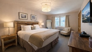 A spacious bedroom with a large bed, a wooden headboard, a chandelier, a chair, a desk with a laptop, and a TV on the wall. - Main Street | Walk to Shopping | Private Balcony (Park City)
