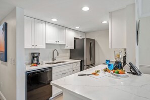 Una cocina moderna con gabinetes blancos, electrodomésticos de acero inoxidable y encimera de mármol.