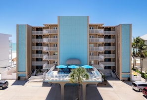 Een meerlaags hotel met een centraal atrium, een terras met parasols en een zwembad.