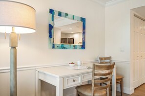 Una habitación con un escritorio blanco, una silla, una lámpara, un espejo y una puerta.