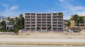 Een meerlaags hotel met een centraal gelegen zwembad, gelegen aan een strand met palmbomen.
