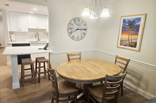 Een moderne keuken met witte kasten, een houten eettafel met vier stoelen, een klok en een lijst met een foto aan de muur.