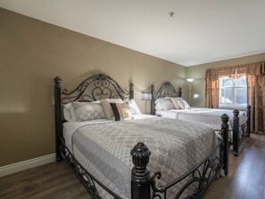 A bedroom with two beds, a window with curtains, and a lamp.