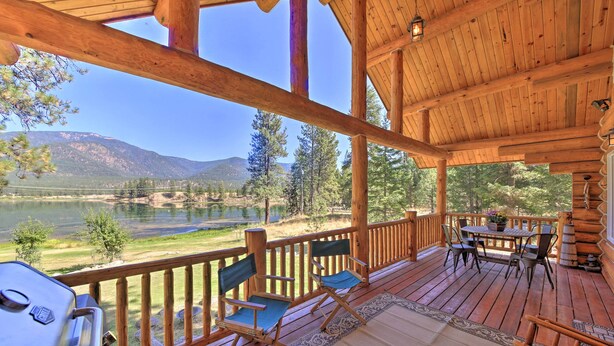 A wooden deck with a grill, chairs, and a table overlooking a lake and mountains. - Scenic Riverfront Retreat w/ Hot Tub & Kayaks! (Thompson Falls)