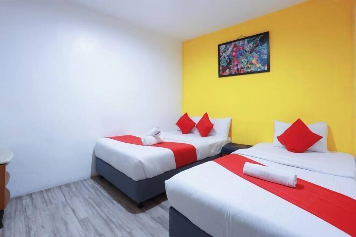 Ein Hotelzimmer mit zwei Betten, jeweils mit roter und weißer Bettwäsche, einer gelben Akzentwand und einem Gemälde über den Betten.