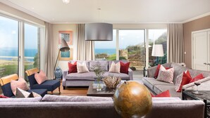A spacious living room with a large grey sofa set, a coffee table with decorative items, and a view of the sea through large windows. - Golden Meadow -  Views - Pet Friendly - Free Parkin - Free WiFi (Torcross)