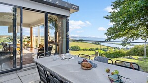 A dining area with a table set for two, overlooking a scenic landscape with a body of water and hills. - Golden Meadow -  Views - Pet Friendly - Free Parkin - Free WiFi (Torcross)
