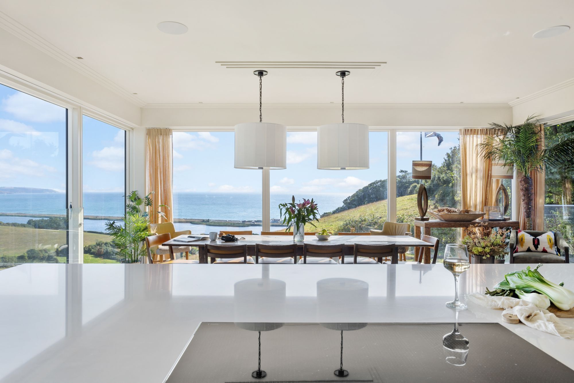 A spacious dining area with a large table, two hanging pendant lights, and a view of the ocean.