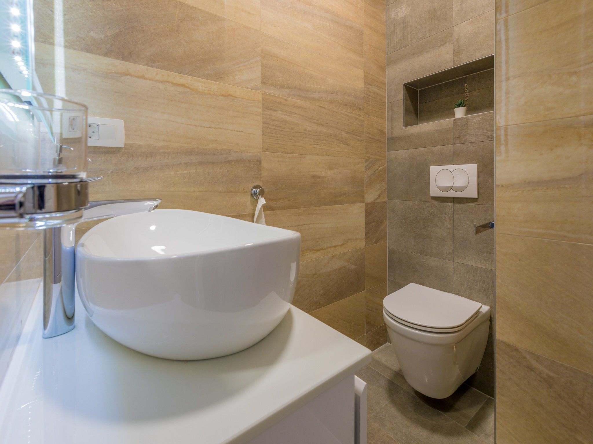 Un baño moderno con un lavamanos grande de color blanco, un inodoro y una pequeña estantería con una planta.