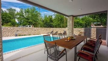 Un espacio al aire libre cubierto con piscina, pared de piedra y una mesa de comedor con sillas.