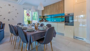 A modern dining area with a table set for four, a kitchen with a large island, and a view of the outdoors through large windows. - Villa Adry (Bribir)