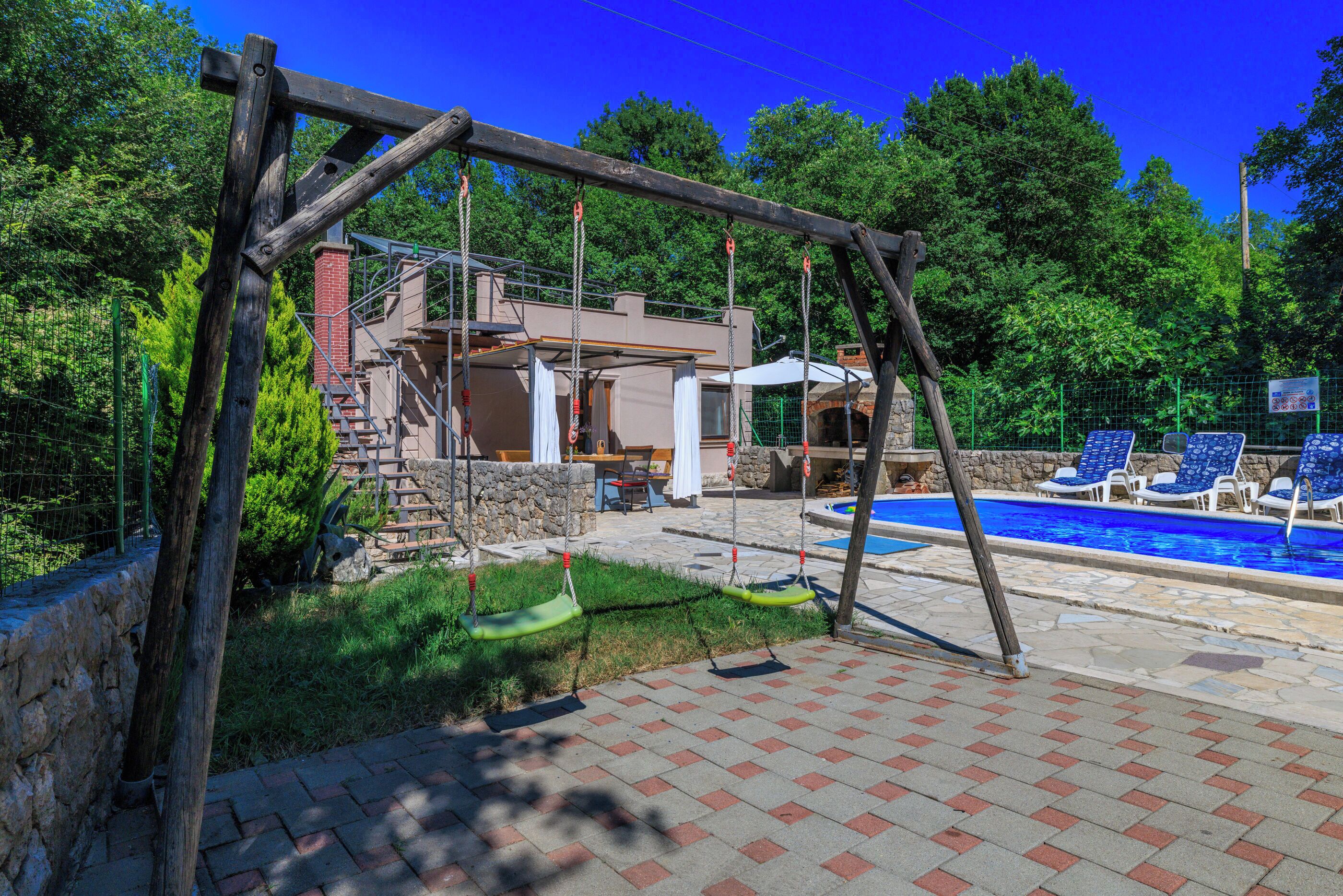 Ein Garten mit Schaukel, Schwimmbecken und einer Terrassenfläche.