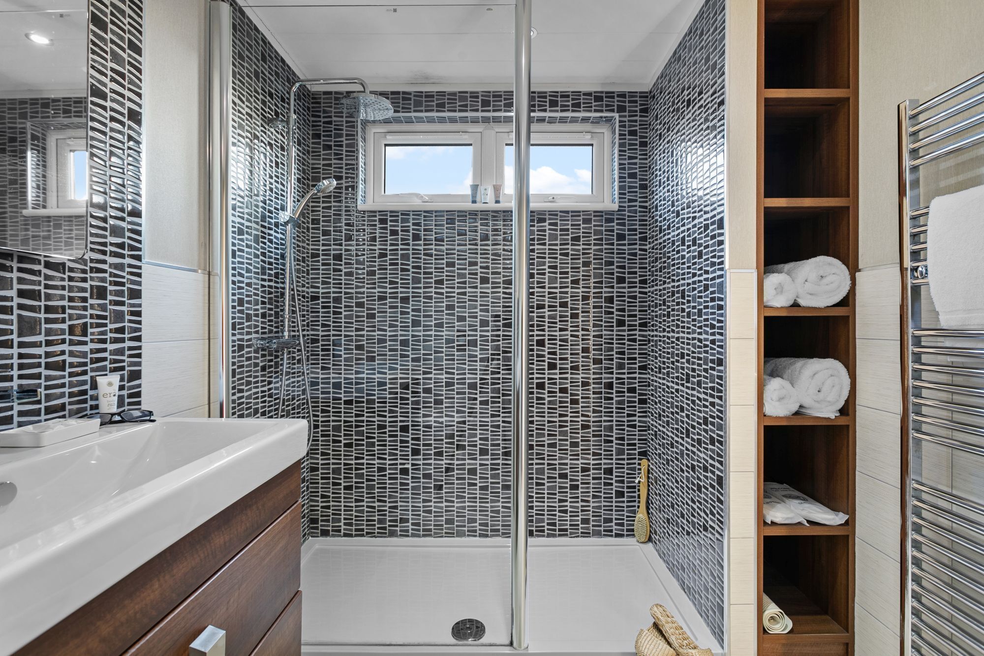 A bathroom with a shower, a window, and a shelf with towels.
