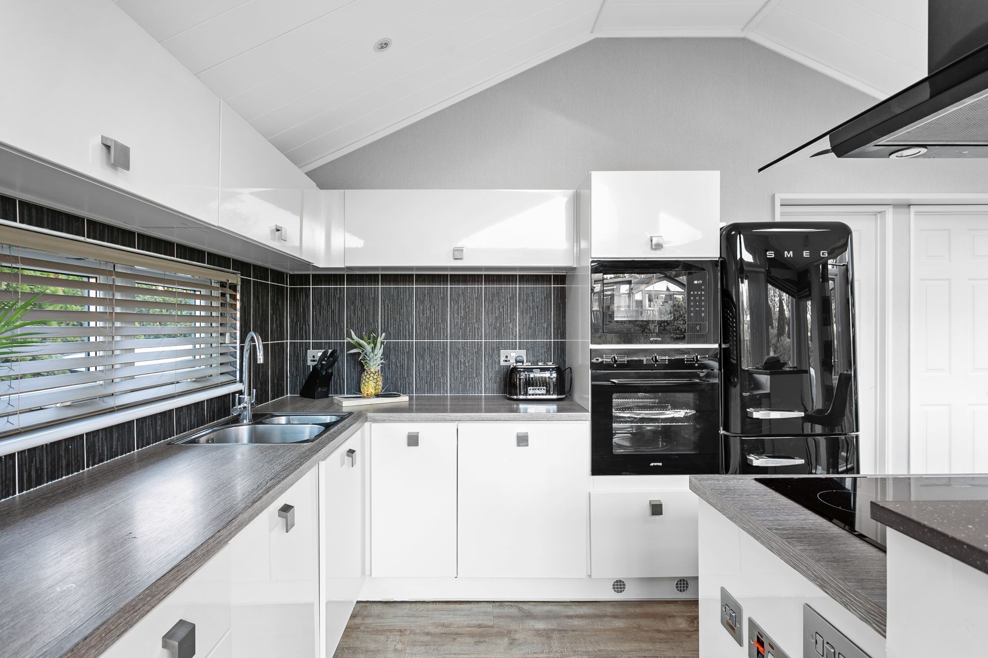 Una cucina moderna con mobili bianchi, un lavello in acciaio inossidabile, un frigorifero nero e un forno integrato.
