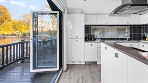 Cocina moderna con armarios blancos, un lavamanos de acero inoxidable y vistas a un lago a través de una puerta de cristal.