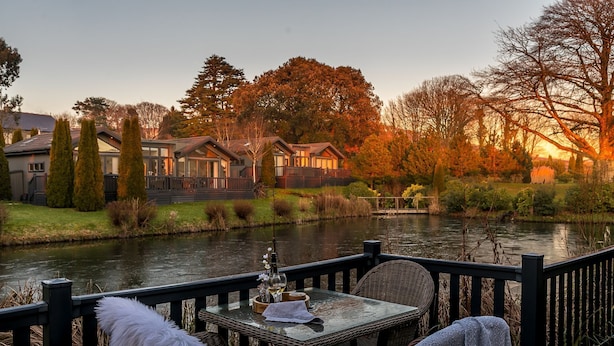 Vista al río con zona de comedor que incluye mobiliario de mimbre y una mesa con una copa de vino.