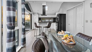 Una cocina moderna con una isla central, taburetes de bar y alimentos para el desayuno sobre una mesa de vidrio.