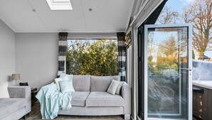 Un salon moderne avec un canapé gris, une table basse sur laquelle sont posés des magazines et un télescope, ainsi qu’une grande porte-fenêtre coulissante donnant sur une terrasse.