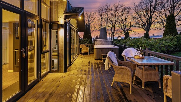 Une terrasse en bois avec des meubles en osier, un jacuzzi et une table dressée pour le repas.