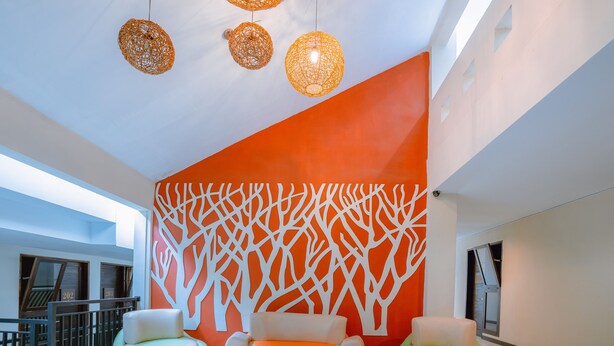 Un vestíbulo moderno con una gran pared naranja, dos sofás verdes e iluminación colgante de mimbre.