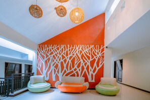 A modern lobby with a large orange wall, two green sofas, and wicker pendant lights.