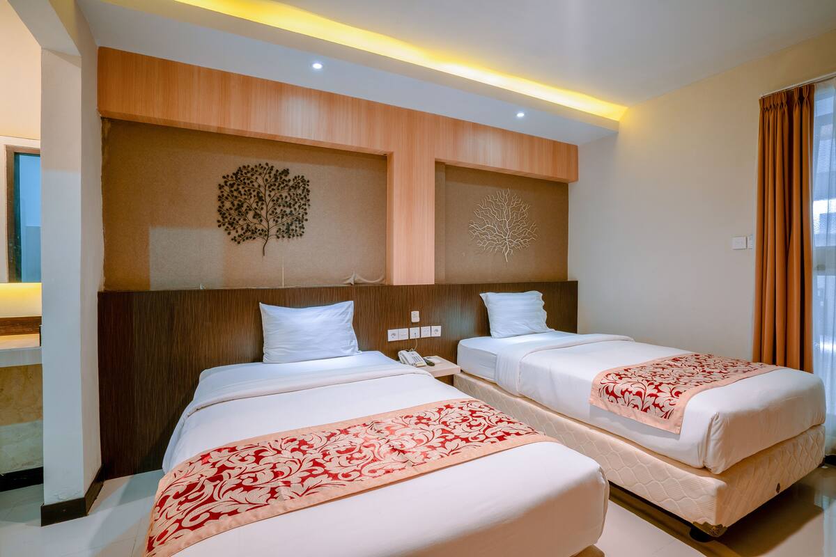 A hotel room with two beds, a wooden headboard, a decorative wall piece, and a window with curtains.