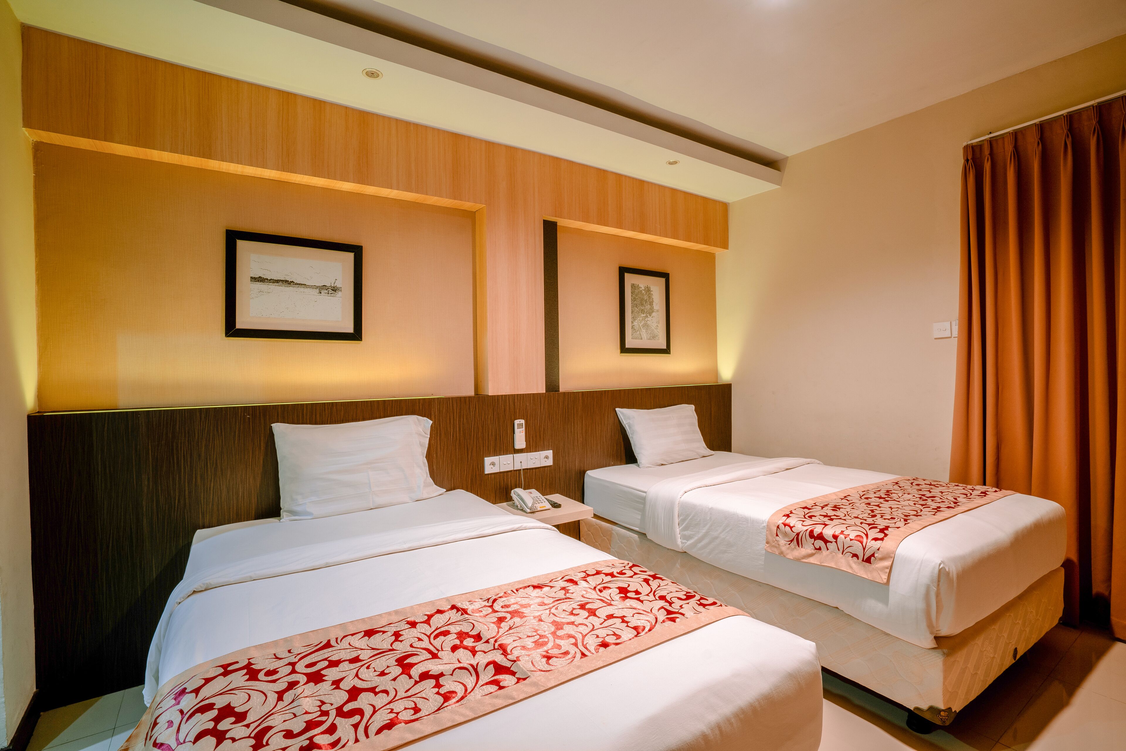 Ein Hotelzimmer mit zwei Betten, Holz-Kopfteilen und gerahmten Bildern an der Wand.