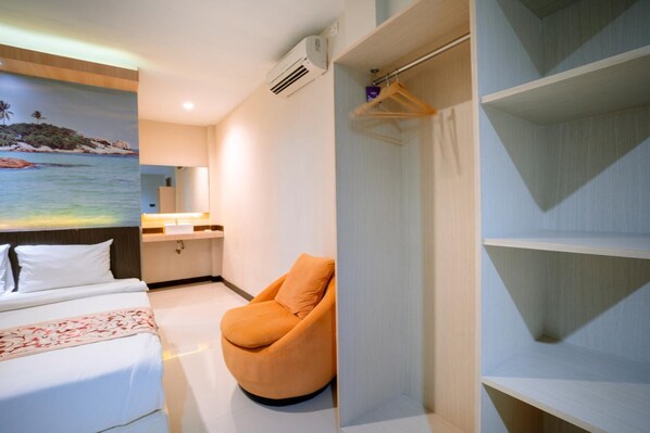 A hotel room with a bed, a chair, a wardrobe, and a painting of a beach scene.