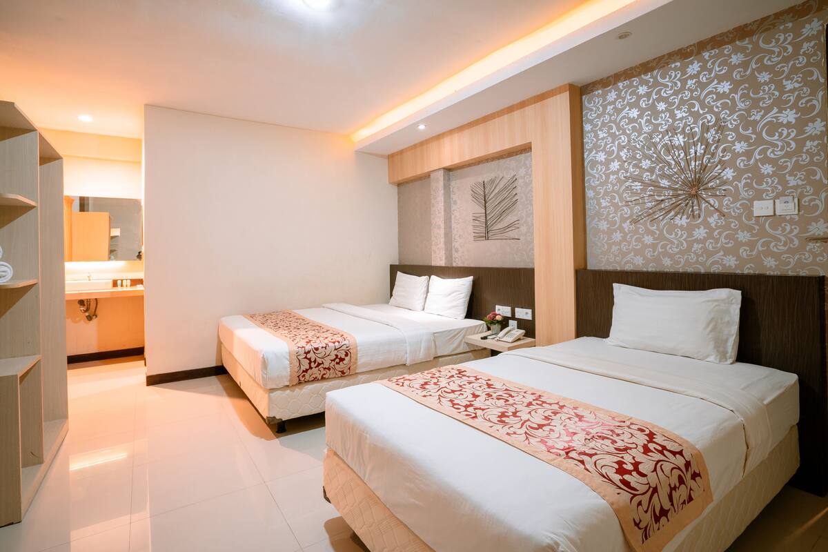 A hotel room with two beds, a wooden headboard, a decorative wall panel, and a bedside table with a phone.