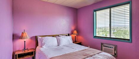 Un dormitorio con cama, dos mesitas de noche con lámparas, un ventilador de techo, una ventana con persianas y un radiador.
