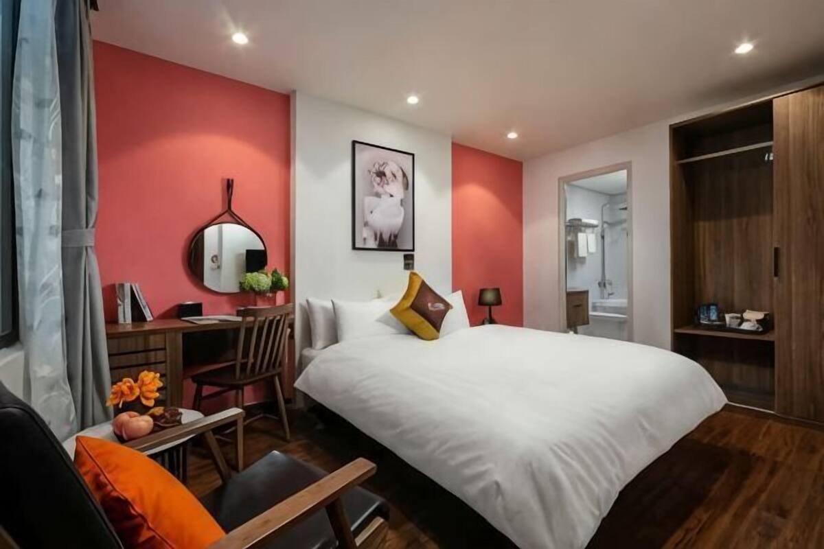 A bedroom with a bed, a desk, a chair, a mirror, and a wardrobe.
