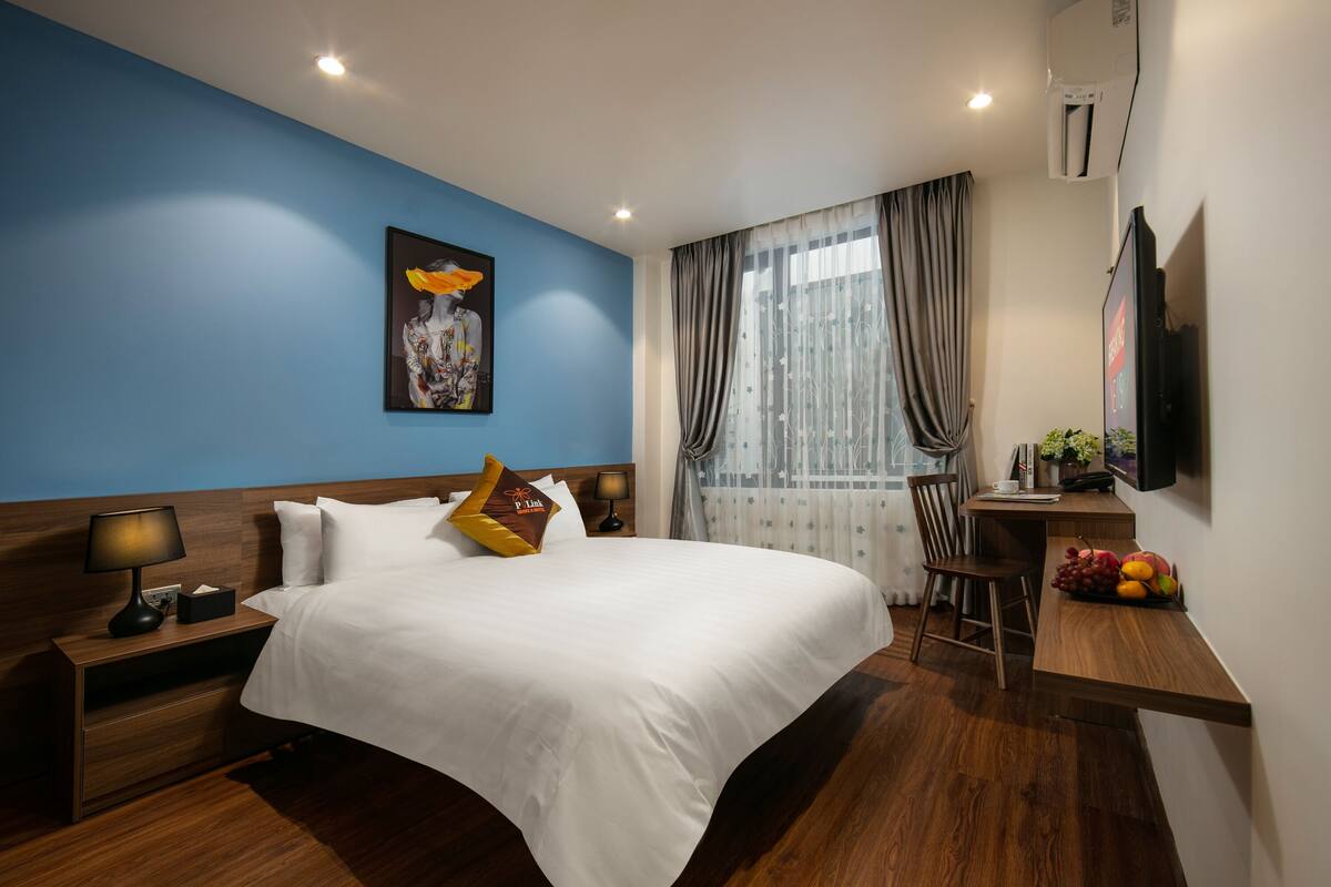 A hotel room with a large bed, a desk with a chair, a television, and a window with curtains.