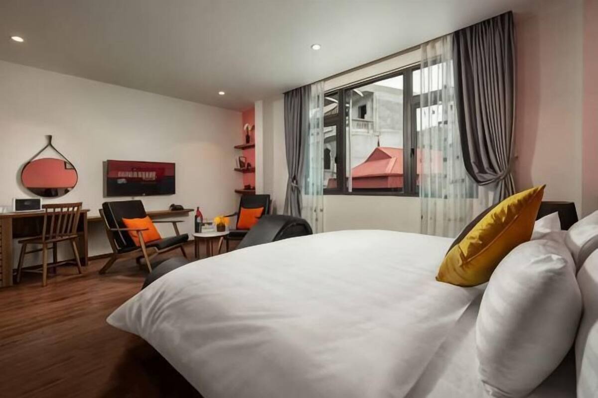 A hotel room with a large bed, a desk with a chair, a television, and a window with curtains.