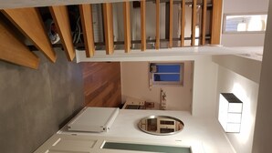A modern interior with a wooden staircase, a small window with blinds, a round mirror, and a built-in shelf.