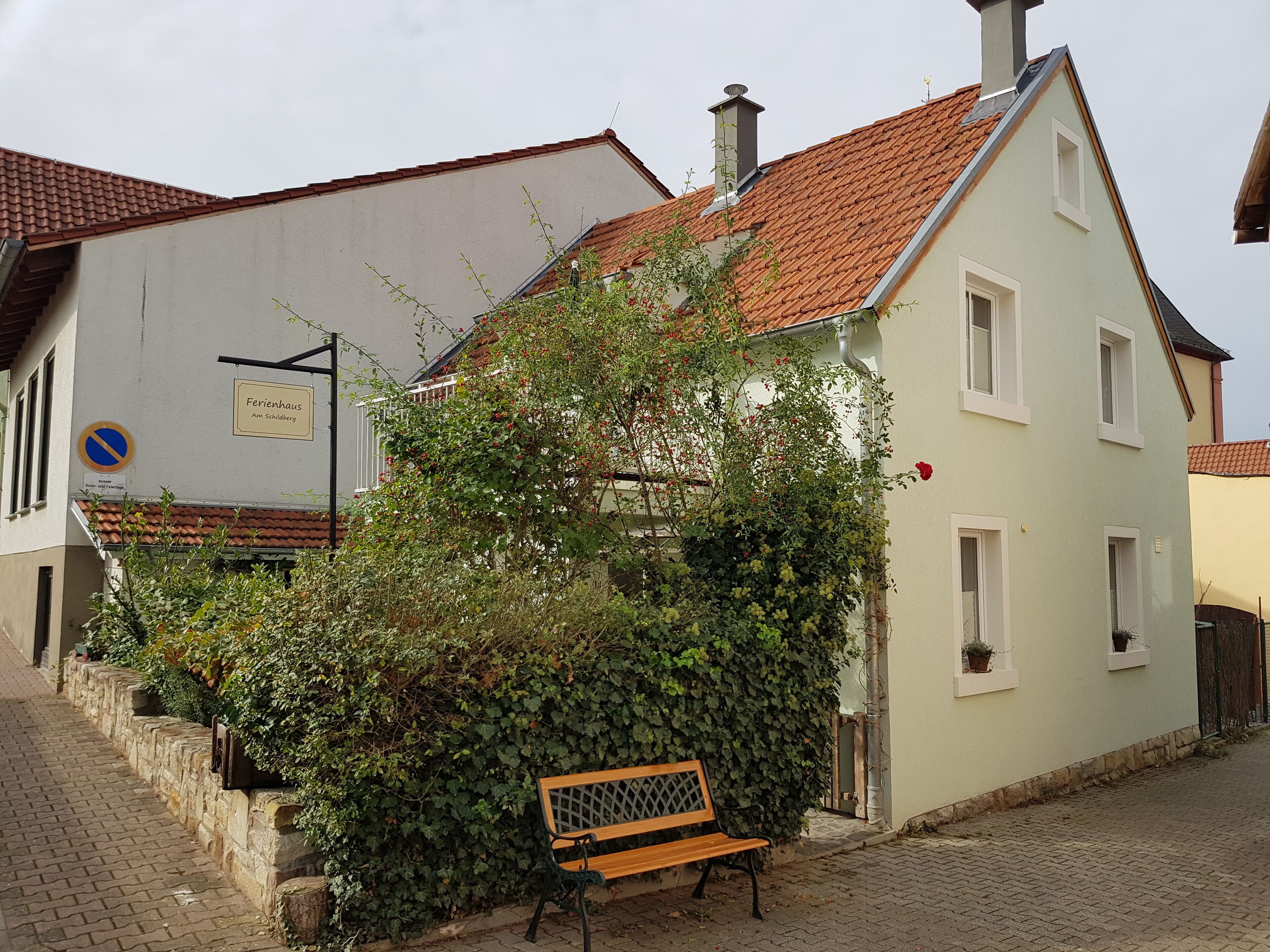 A building with a sign reading "Ferienhaus Am Schilberg" and a bench in front.