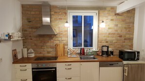 A compact kitchen with a brick wall, a stainless steel range hood, a built-in oven, a dishwasher, and a microwave.