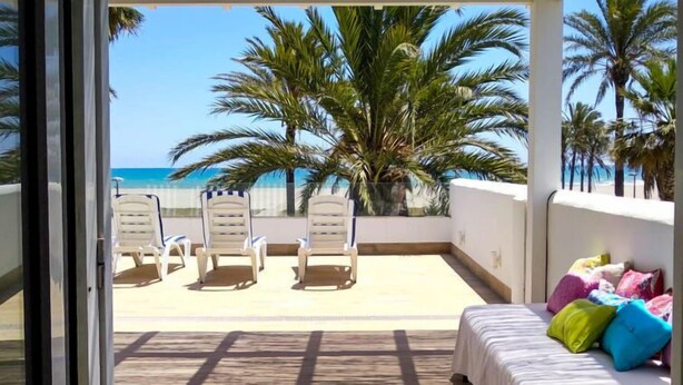 Ein Balkon mit einem Bett, einem Sessel und Blick auf den Strand.