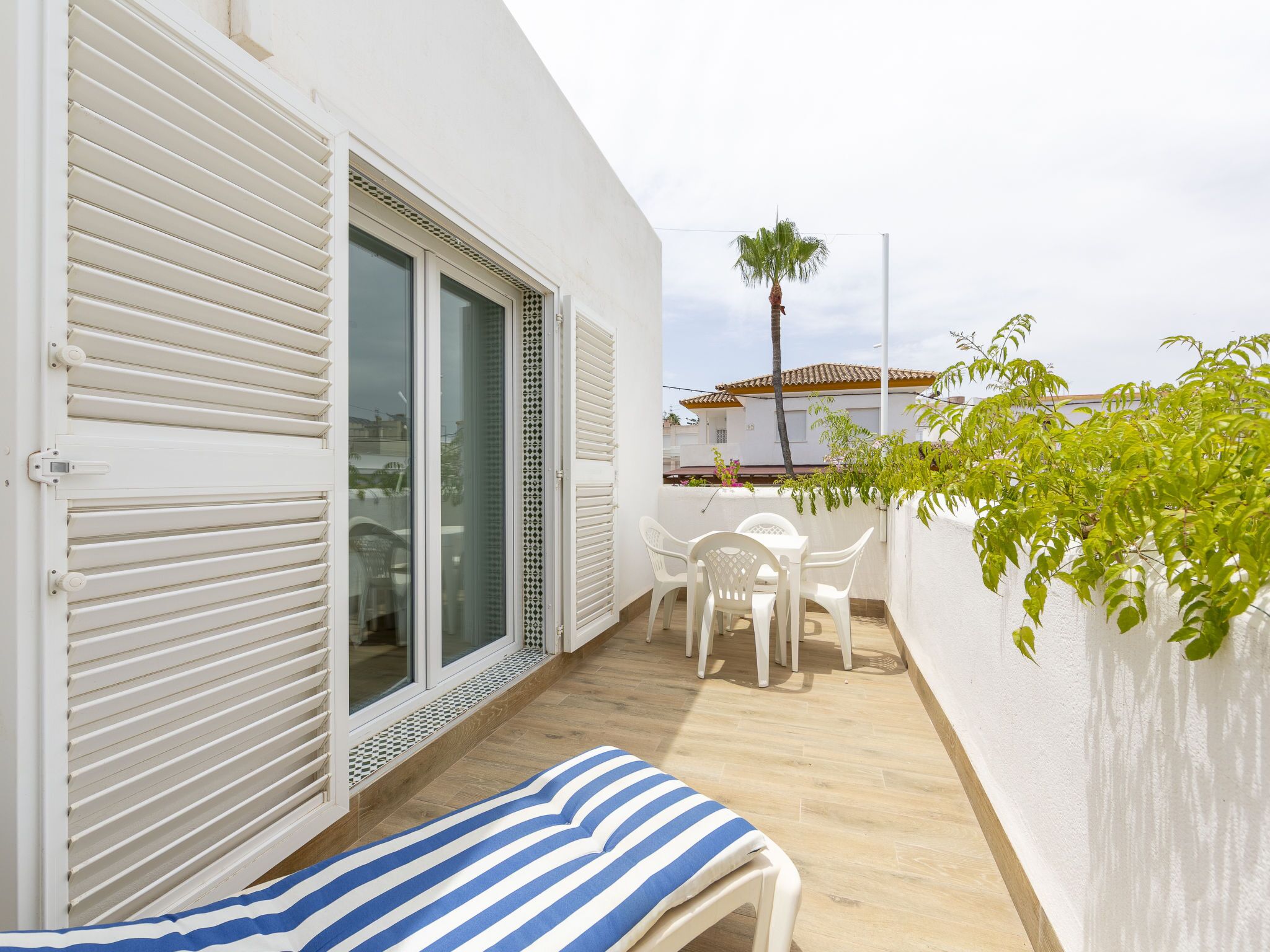 Un balcon avec une chaise blanche, une petite table et un coussin à rayures.