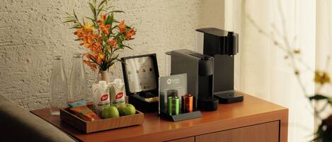 A wooden desk with a vase of flowers, a framed picture, a coffee maker, and a tray of snacks.