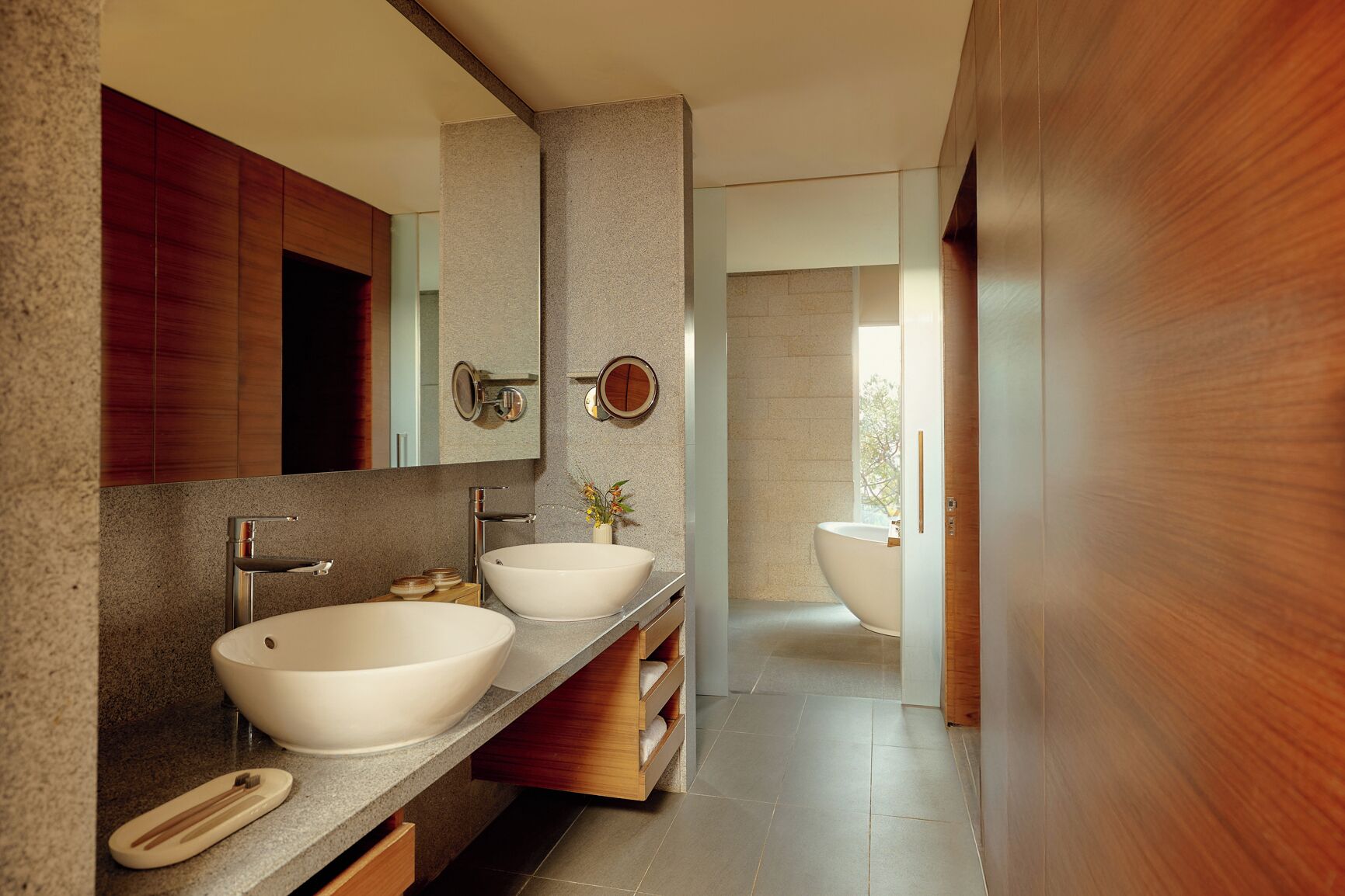 A modern bathroom with two sinks, a large mirror, and a bathtub.