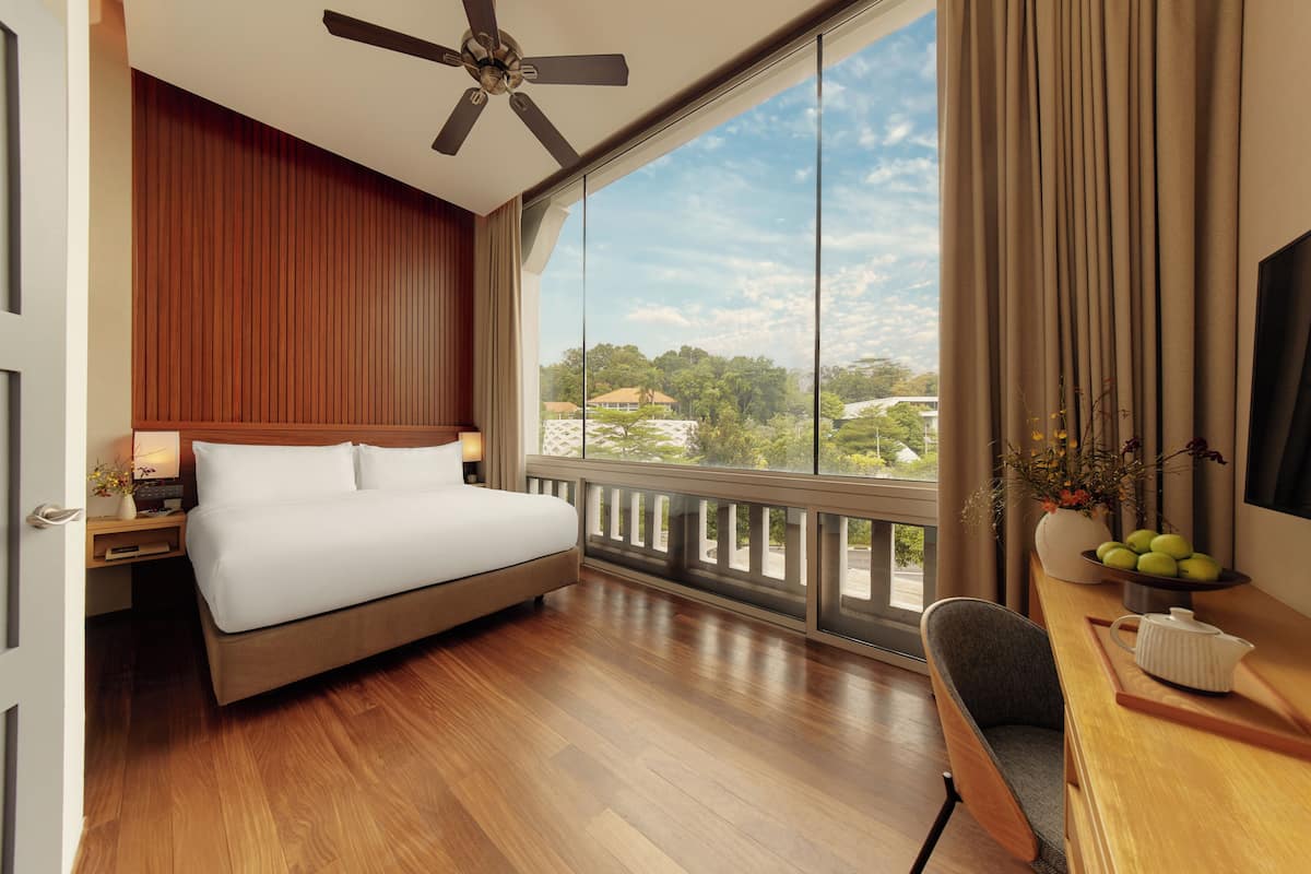 Une chambre d’hôtel comprenant un lit, un bureau avec une chaise, une télévision, un ventilateur de plafond et une grande fenêtre donnant sur l’extérieur.