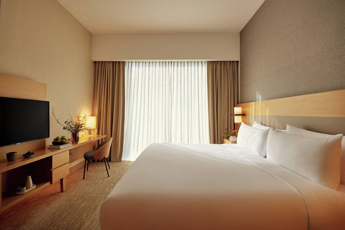 Une chambre d’hôtel avec un lit, un bureau avec une télévision, une chaise et une fenêtre avec des rideaux.