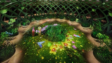 An indoor garden with a central circular area surrounded by pathways and potted plants.