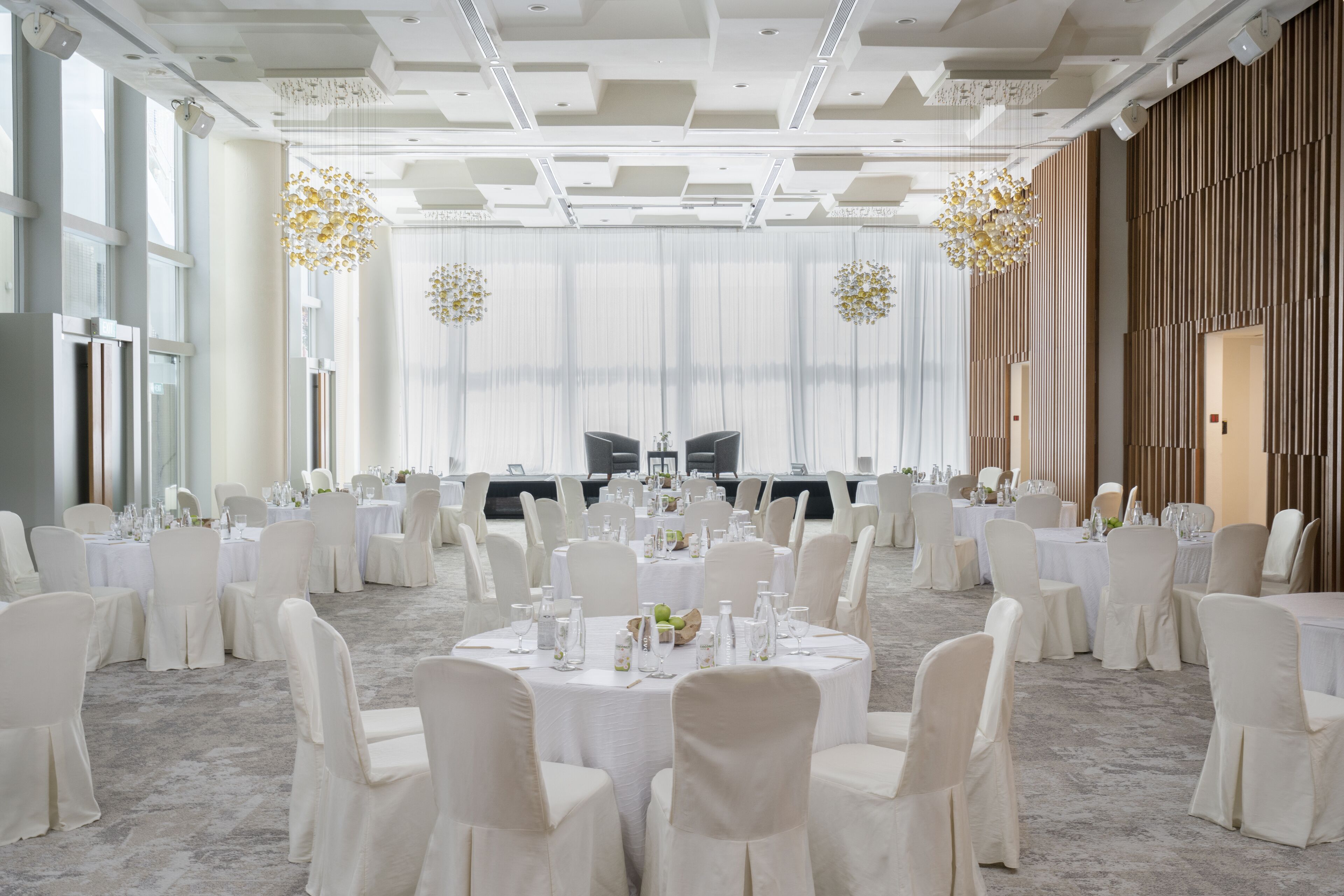 Un salón de banquetes con mesas redondas, sillas blancas y candelabros.
