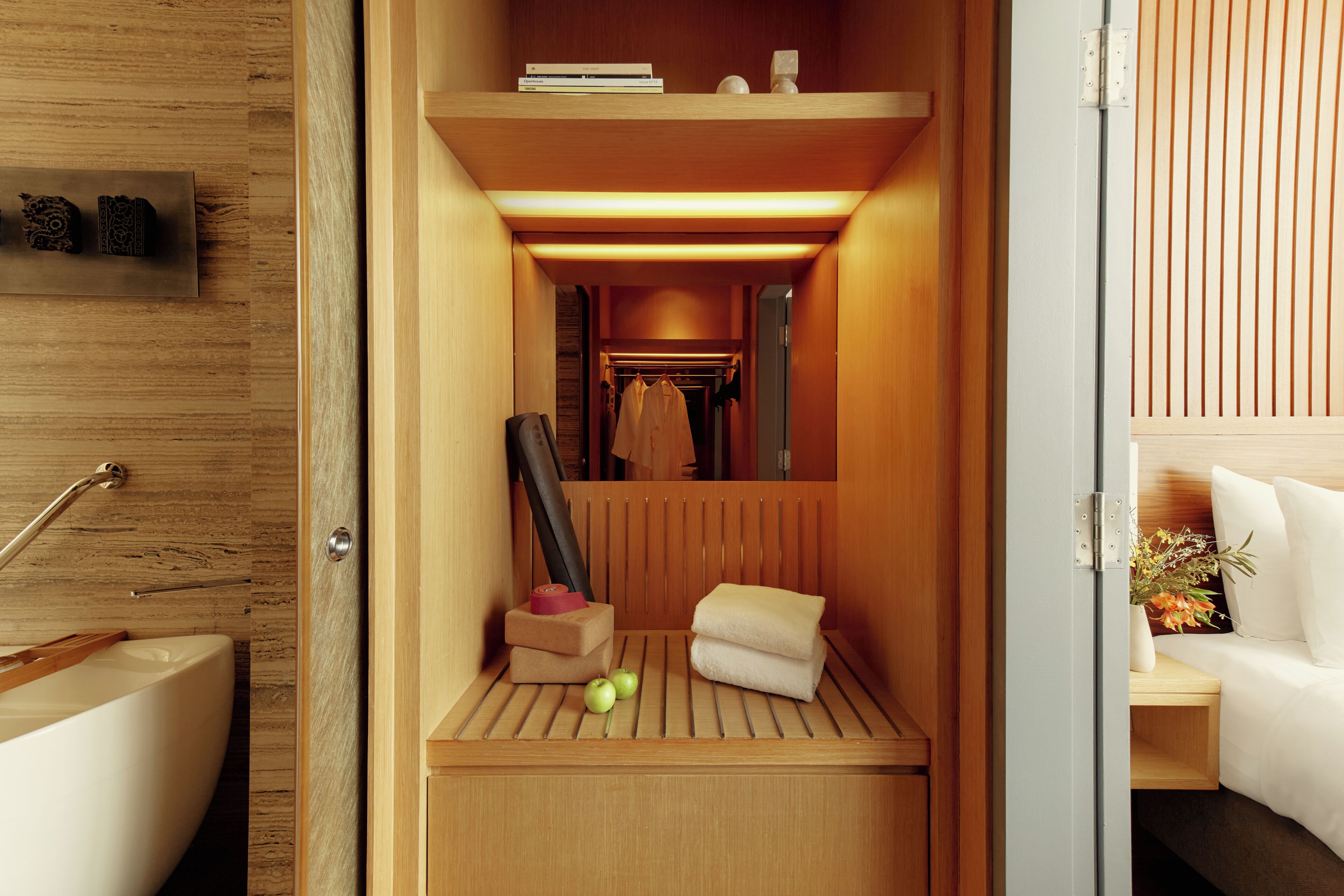 A compact room with a wooden floor, a small bed, a bedside table with a vase, and a mirror.