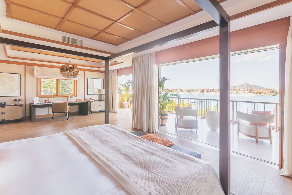 A spacious bedroom with a large bed, a desk, and a balcony with a view of the sea.