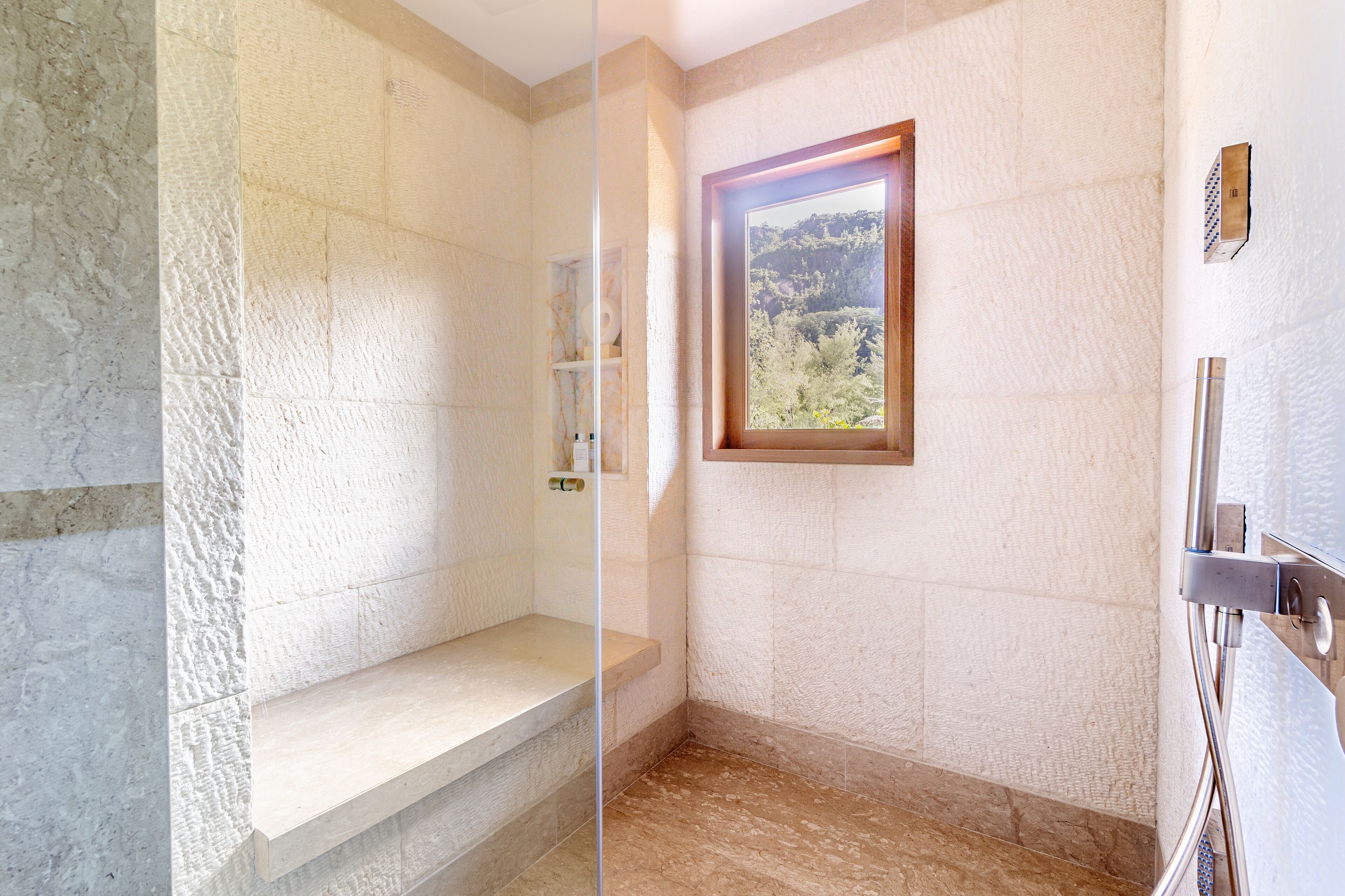 A bathroom with a stone wall, a bench, a framed picture, and a shower area.