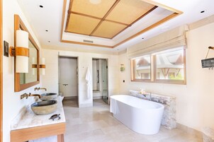 Un baño moderno con una bañera grande, dos lavamanos con cuencos de piedra, un espejo amplio y vistas al exterior a través de una ventana.