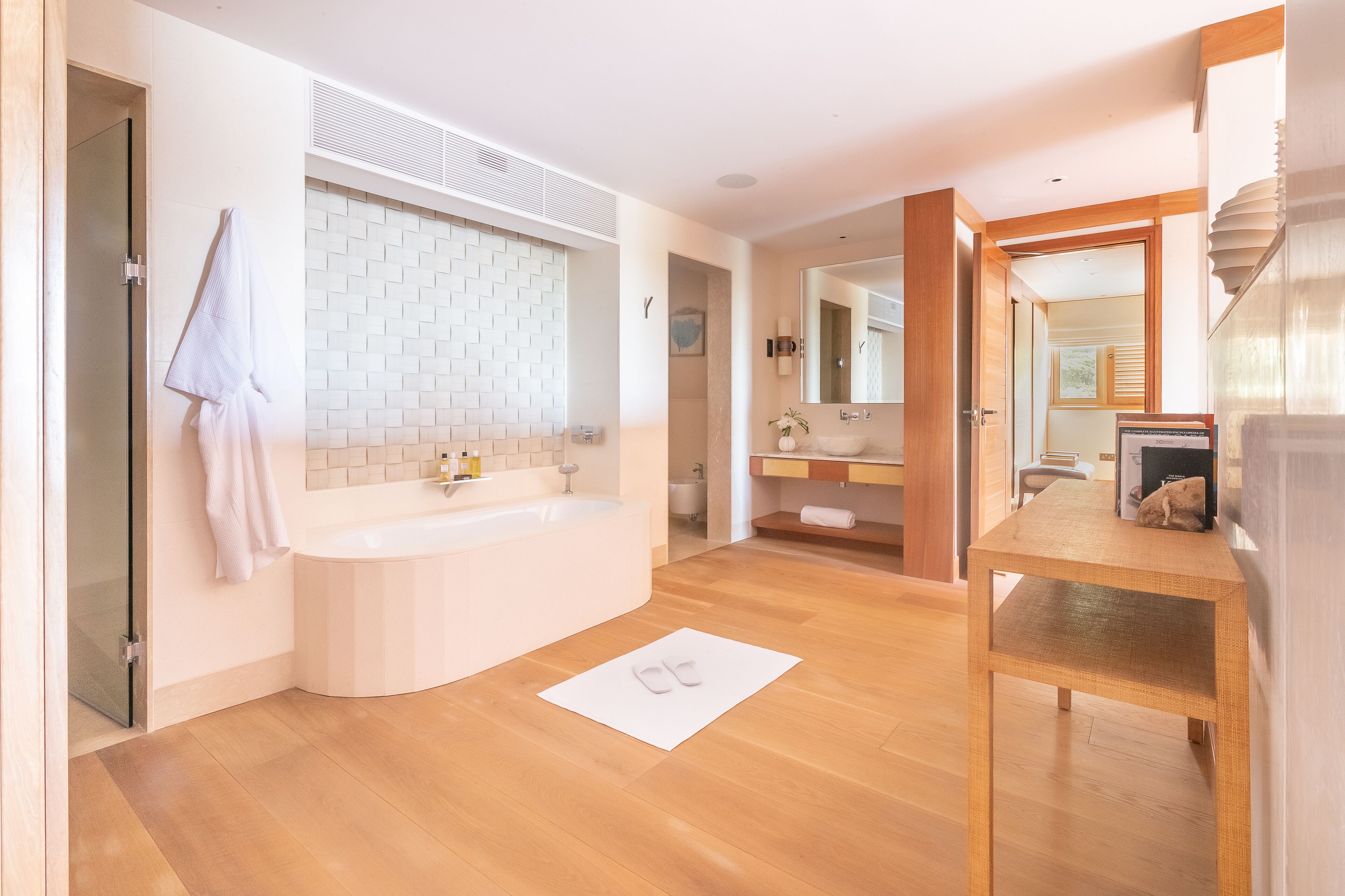Un baño moderno con una bañera independiente, un espejo grande y un mueble de tocador de madera.