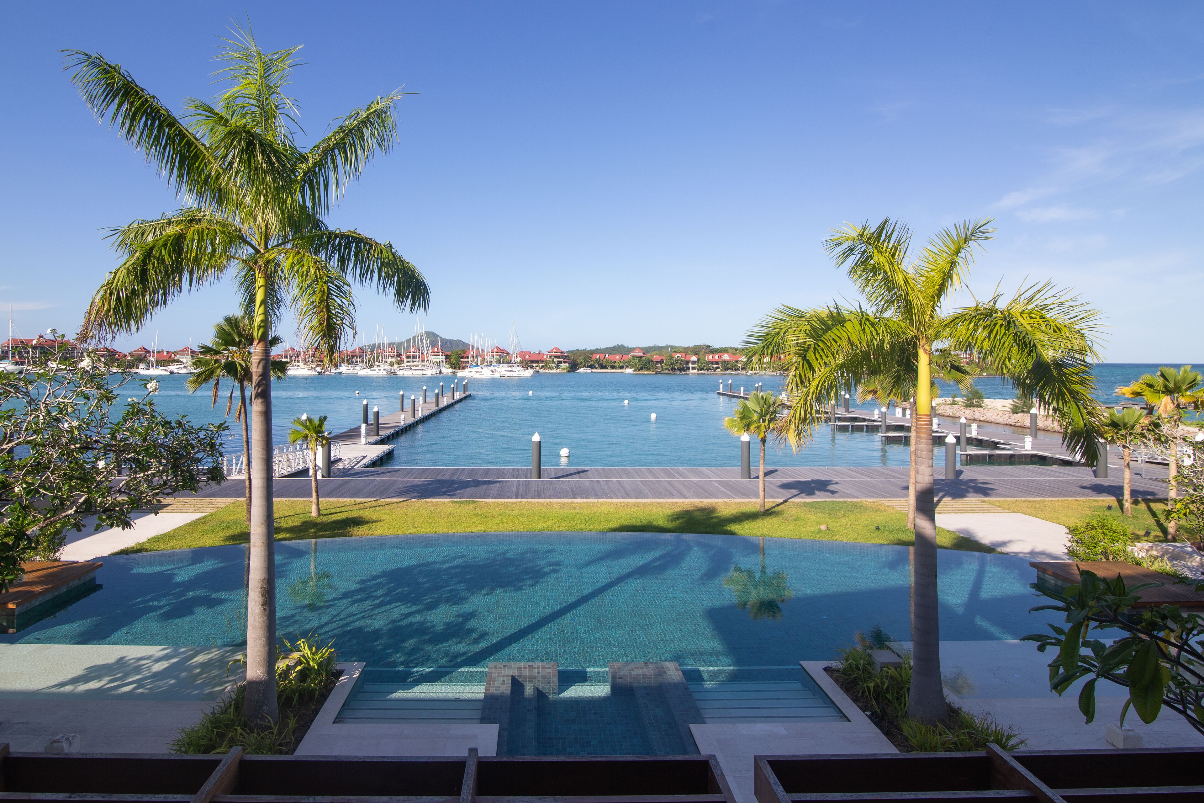 Un espace piscine offrant une vue sur le port de plaisance, entouré de palmiers et surplombé d’un ciel bleu azur.